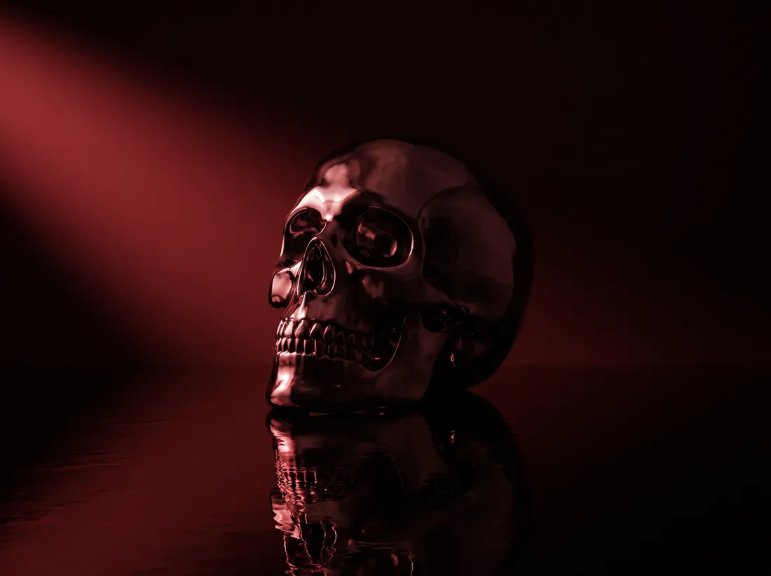 A polished chrome skull on a wet black floor under raking red light.